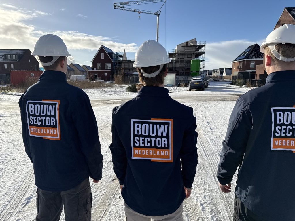 Drie vakmensen van Bouwsector Nederland met witte helm op een bouwplaats in de sneeuw